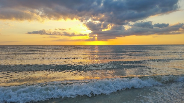Un atardecer sobre un mar tranquilo con olas acariciando suavemente la orilla.
