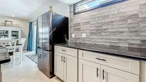 Una cocina moderna con un refrigerador de acero inoxidable, armarios blancos y un salpicadero de ladrillo.
