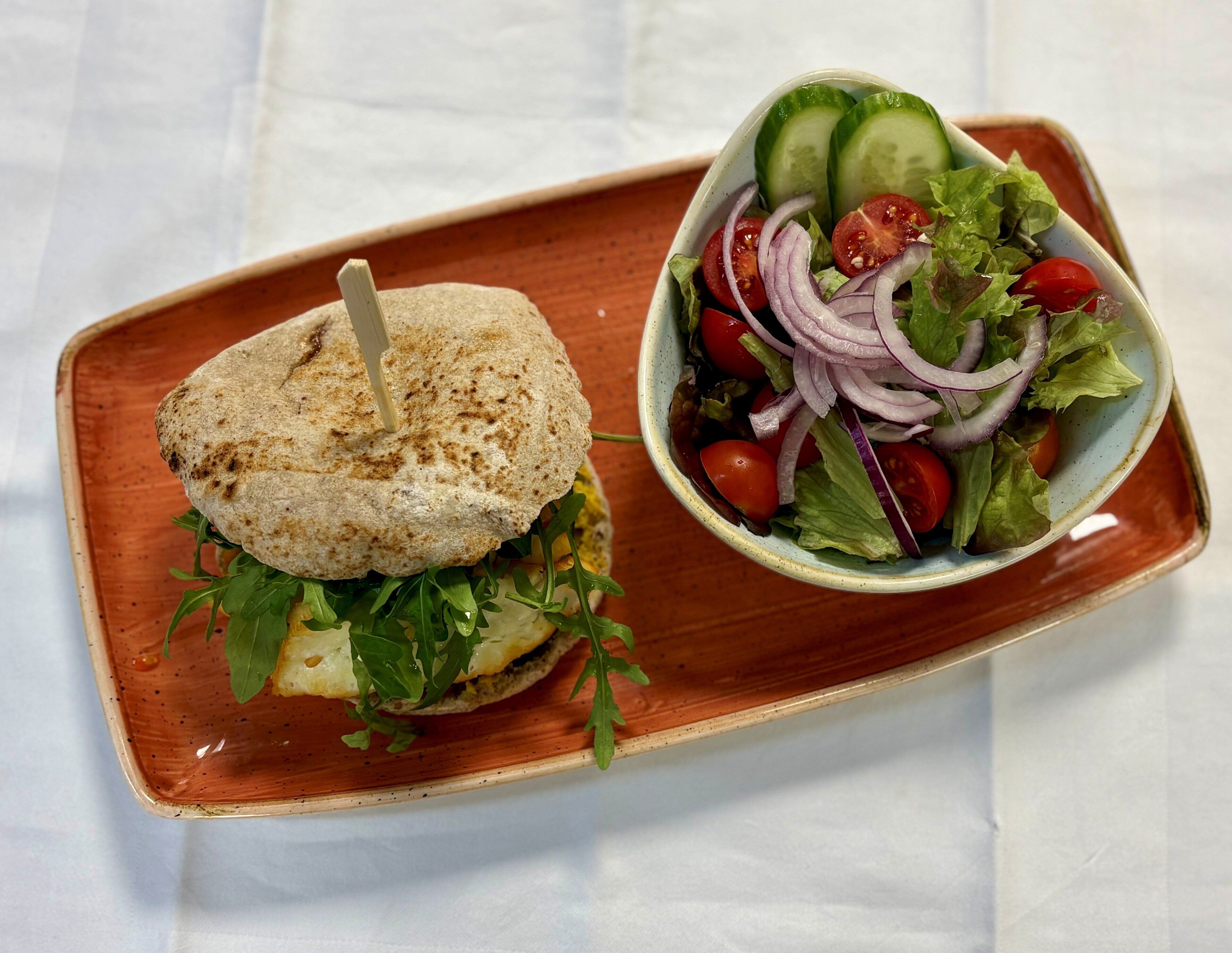 A sandwich with a toothpick on a plate next to a bowl of salad.