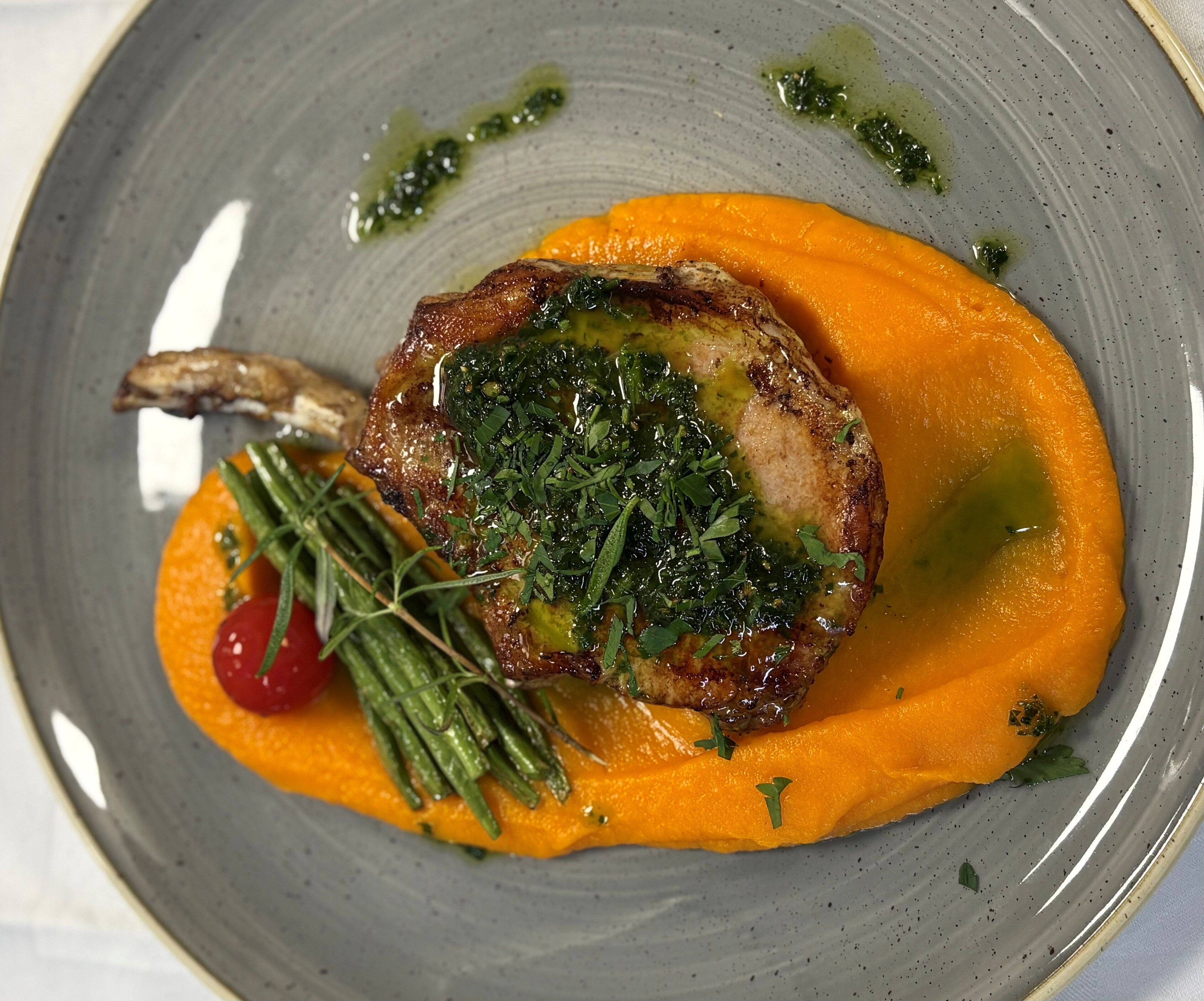 Un plato con carne a la parrilla, una rodaja de naranja y hierbas como guarnición.
