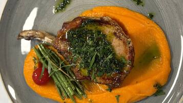 Un plato con carne a la parrilla, una rodaja de naranja y hierbas como guarnición.