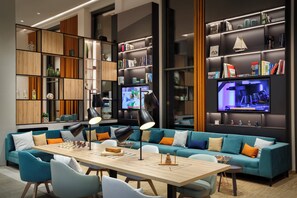 A modern living room with a large sofa, a dining table, and built-in bookshelves. - Holiday Inn Hamburg - Hafencity by IHG (Hamburg)