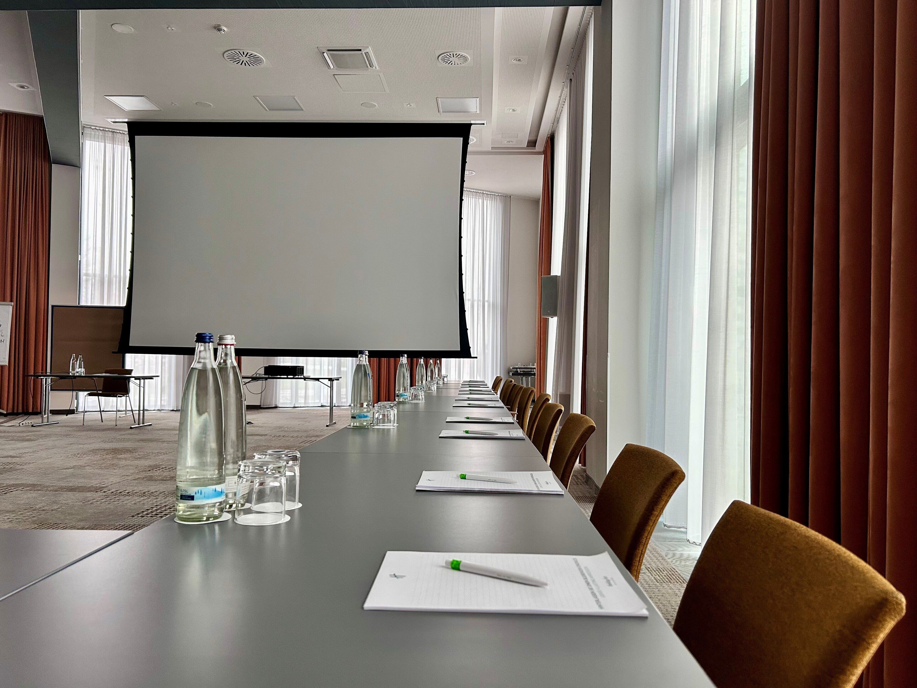 A conference room with a long table, chairs, a projector screen, and a whiteboard.