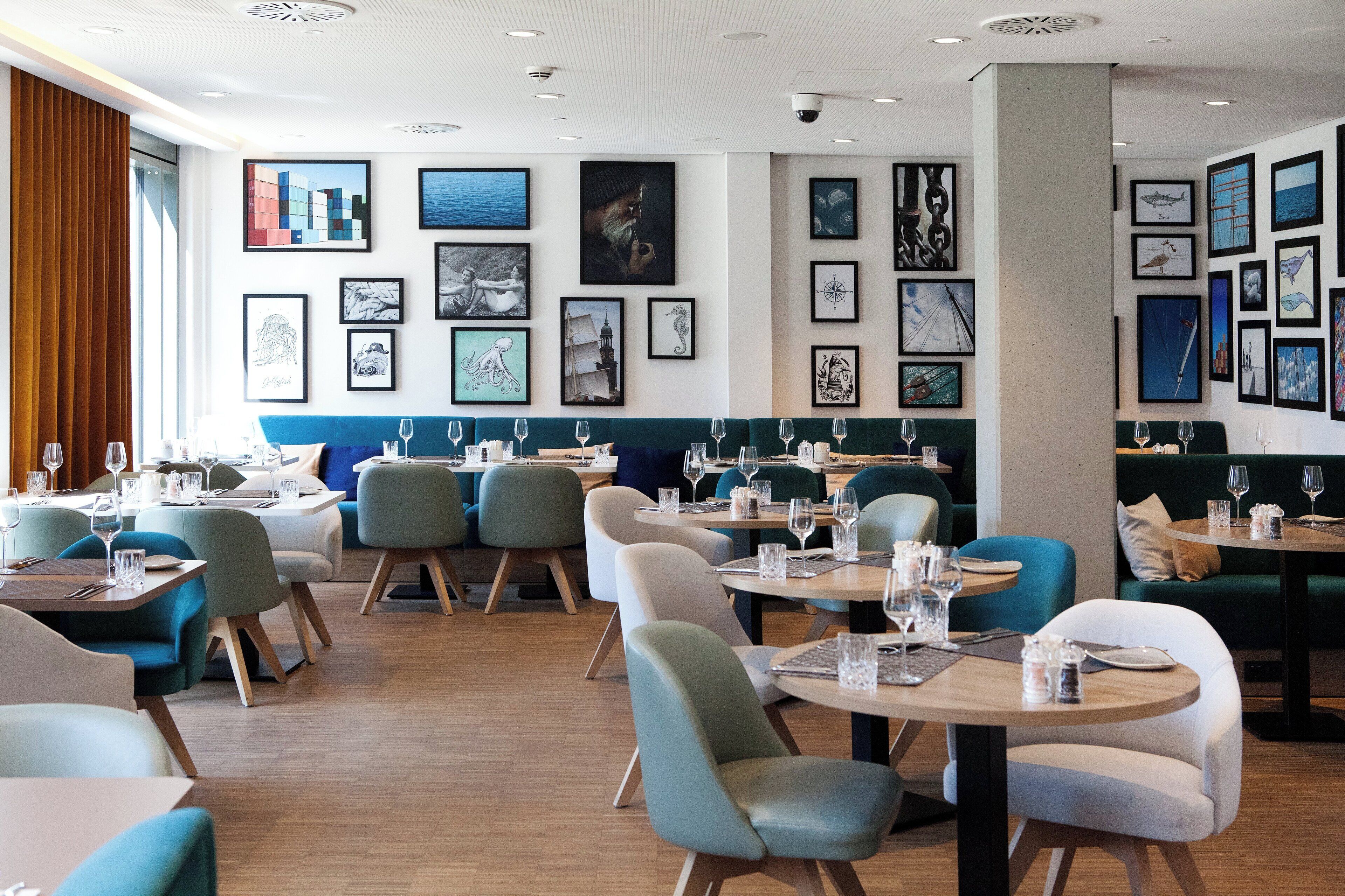 Un interior de restaurante moderno con varias mesas y sillas para comer, obras de arte enmarcadas en las paredes y suelo de madera.
