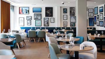 Un interior de restaurante moderno con varias mesas y sillas para comer, obras de arte enmarcadas en las paredes y suelo de madera.
