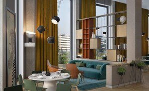 Ein modernes Wohnzimmer mit einem petrolfarbenen Sofa, einem Esstisch mit Stühlen und einem Bücherregal.