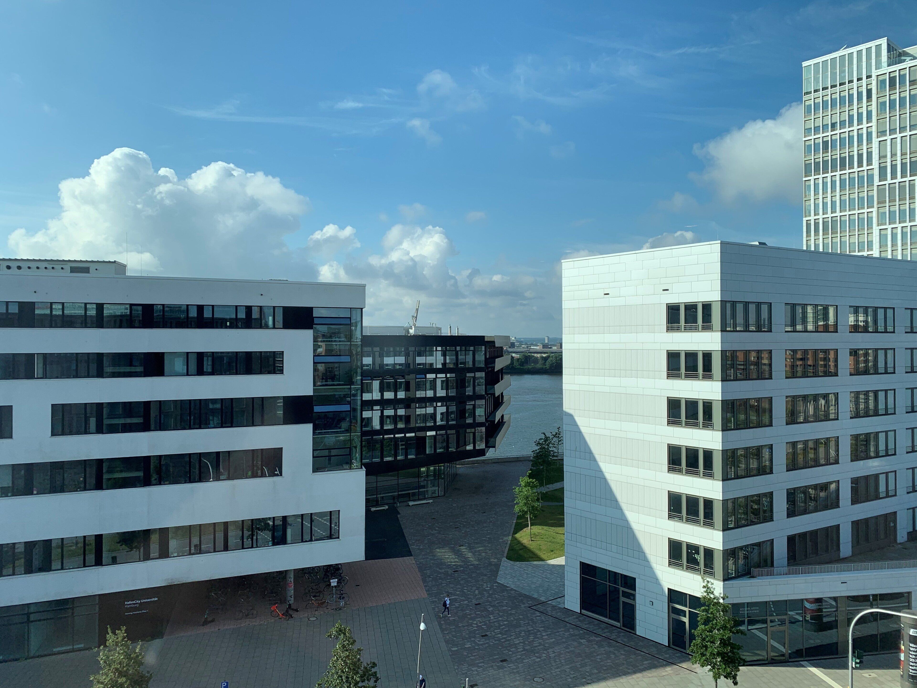 A modern building with multiple floors and large windows, situated near a river.