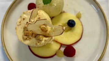A dessert plate with a scoop of ice cream, apple slices, a blueberry, and a mint leaf.