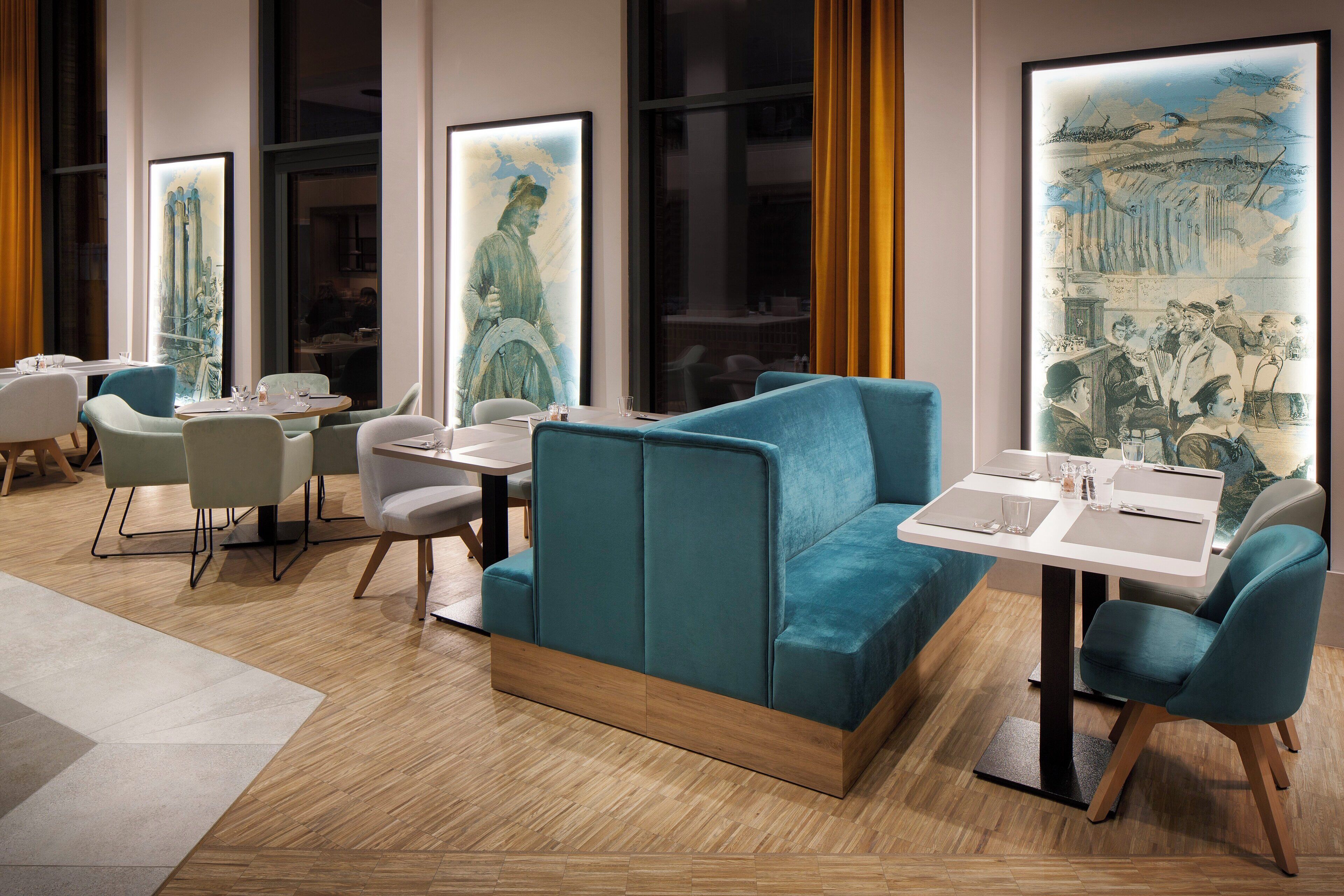 Un comedor moderno con asientos tapizados en color turquesa, suelo de madera y ventanas amplias con obras de arte.