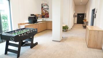 Un moderno vestíbulo de hotel con una mesa de fútbol de mesa, una zona de cocina y un mostrador de recepción.