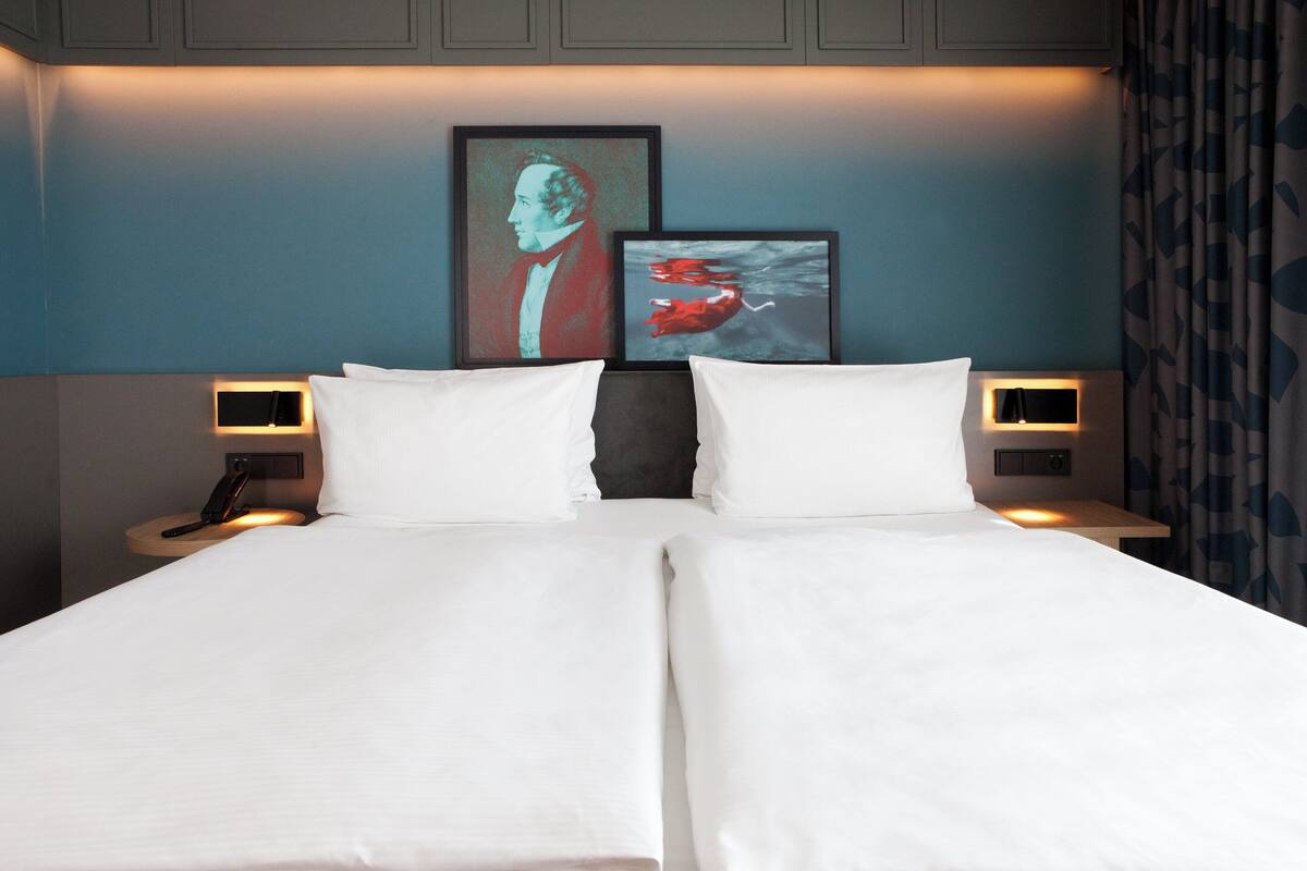 A double bed with white linens, two bedside tables with lamps, and two framed artworks on the wall.