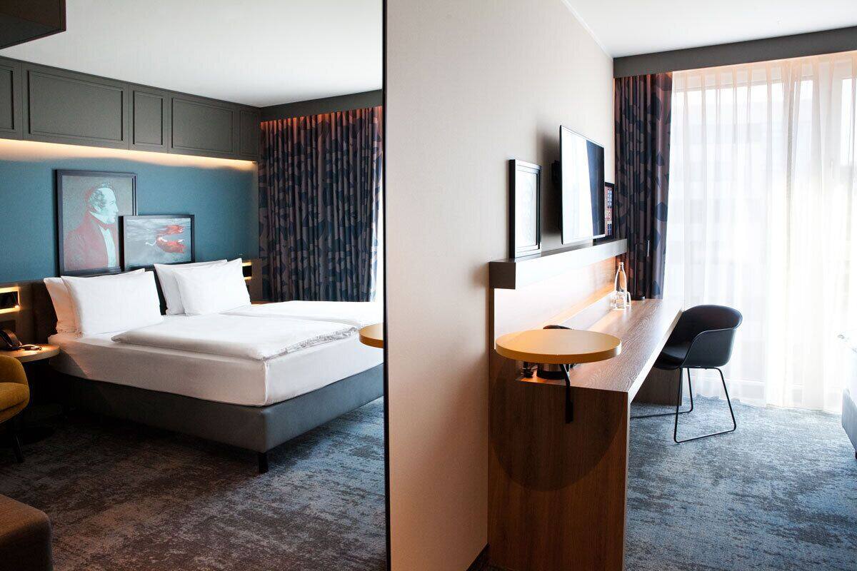 A modern hotel room with a large bed, a desk, a chair, and a television.