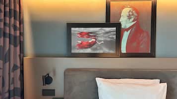 Habitación de hotel con cama, mesita de noche, un cuadro con la imagen de un hombre y un cuadro con la imagen de una mujer.