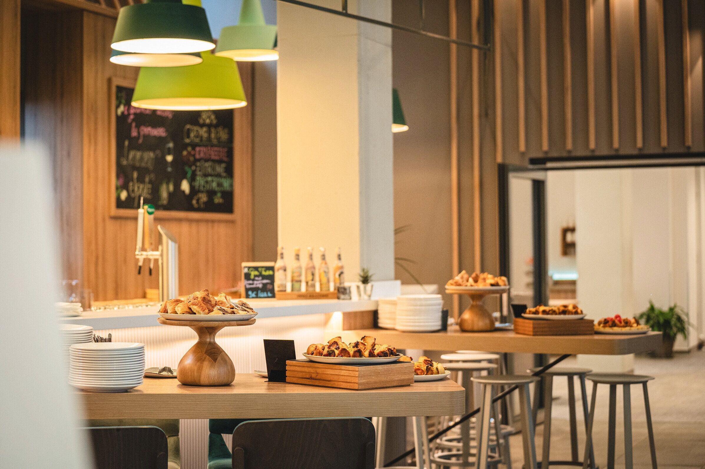 A modern restaurant interior with wooden tables, green pendant lights, and a chalkboard menu.