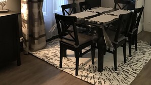 Un coin repas comprenant une table rectangulaire, six chaises, un tapis à motifs, une lampe et un luminaire au plafond.