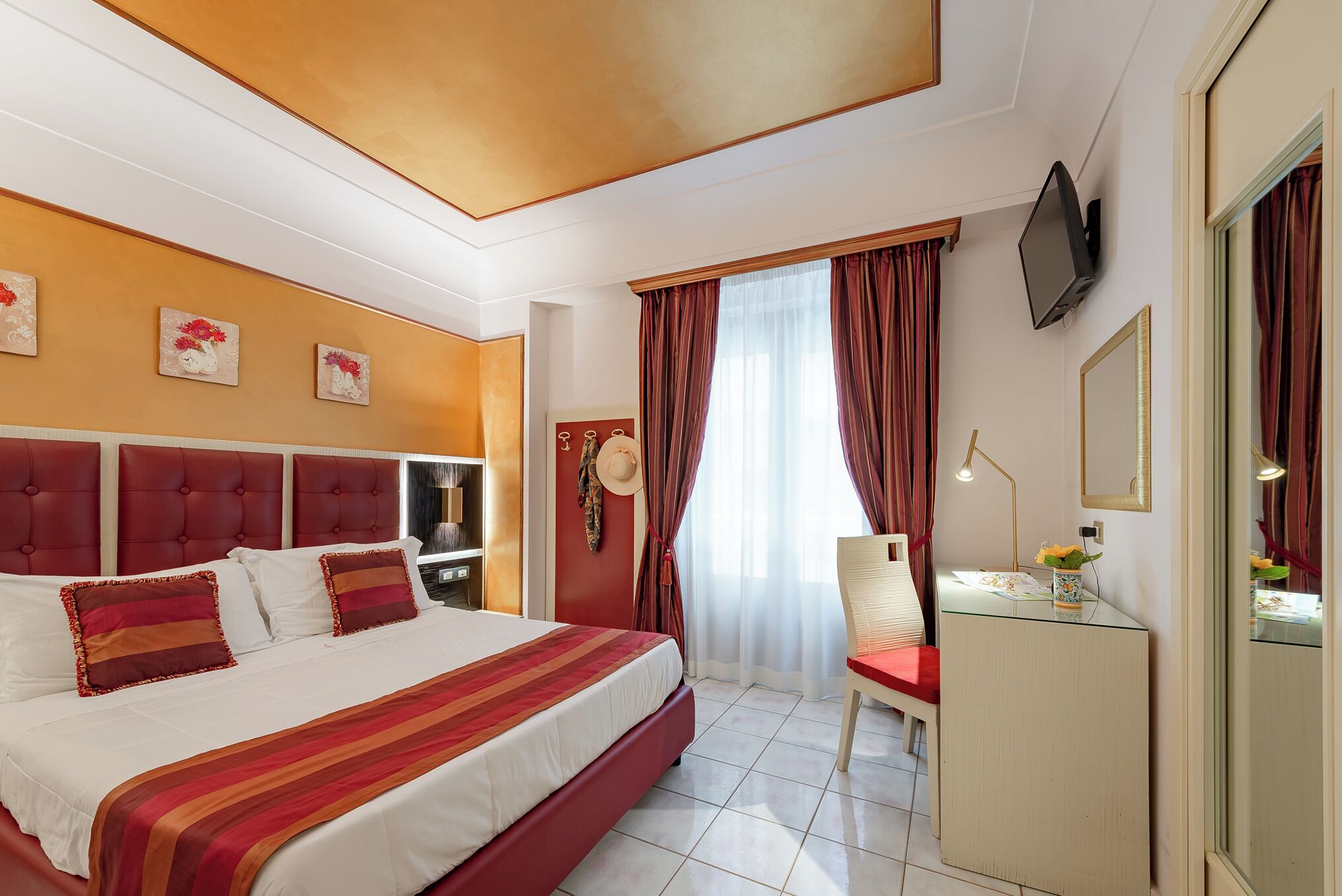 A hotel room with a large bed, a desk with a chair, a TV, and a window with curtains.