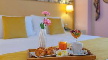 Een ontbijfwagen met croissants, een glas sinaasappelsap, een kop koffie en een schaal fruit op een bed met kussens en een wandklok.