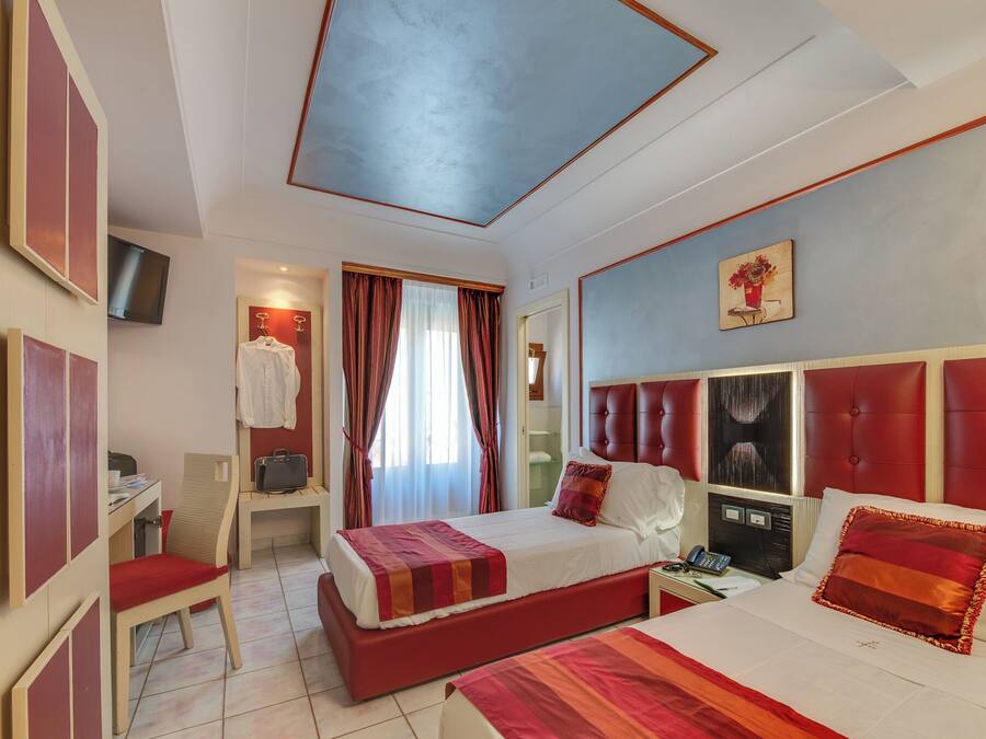 Habitación de hotel con dos camas, un escritorio, una silla, un televisor y un cuadro en la pared.