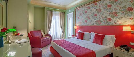 Habitación de hotel con una cama grande, un escritorio con lámpara, una silla y un ventanal con cortinas.