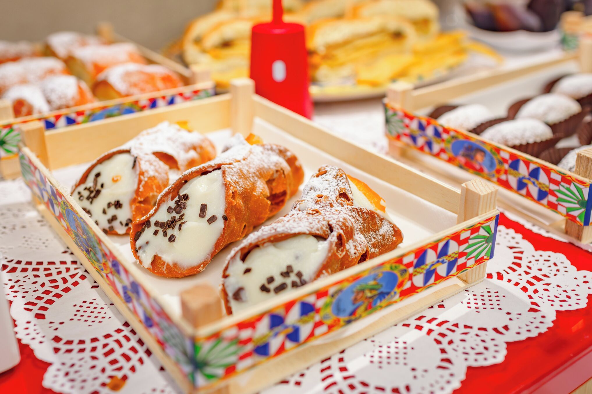 A table with various pastries and desserts, including cannoli and cupcakes, arranged in colorful boxes.