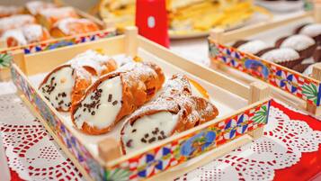 A table with various pastries and desserts, including cannoli and cupcakes, arranged in colorful boxes.