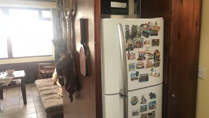Une cuisine avec un réfrigérateur recouvert d’aimants, un meuble en bois, un canapé et une fenêtre.