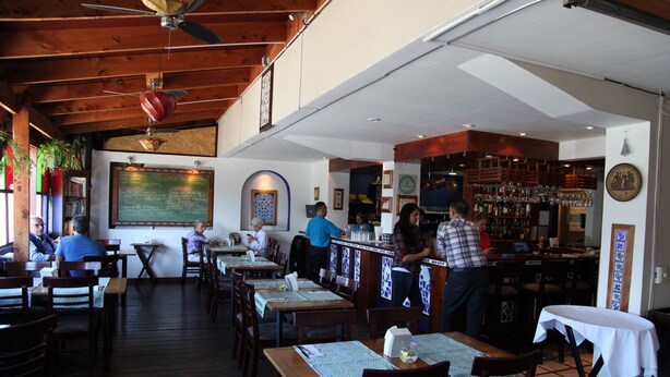 Un restaurant avec des tables et des chaises en bois, un coin bar et un menu écrit à la craie.
