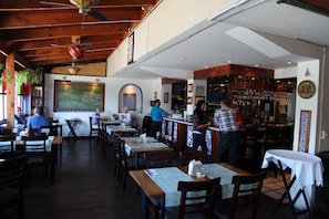Un restaurante con mesas y sillas de madera, una zona de bar y un menú en una pizarra.