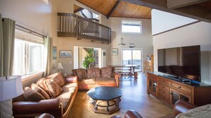 A spacious living room with a high ceiling, a large TV, and a staircase leading to an upper level. - Pajaro Dunes House 81 (Watsonville)
