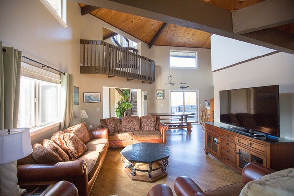 A spacious living room with a high ceiling, a large TV, and a staircase leading to an upper level. - Pajaro Dunes House 81 (Watsonville)