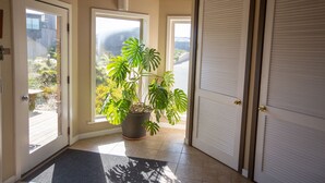 A hallway with a potted monstera plant, a door with a window, and a closed door with a window. - Pajaro Dunes House 81 (Watsonville)