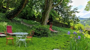 Un jardin luxuriant avec un hamac, des chaises rouges et blanches, et une table.
