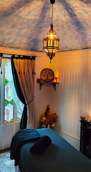 A bedroom with a bed, a hanging light fixture, a wall-mounted shelf with a decorative item, and a window with curtains.