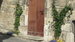 Un bâtiment en pierre avec une porte double en bois, une petite plaque au-dessus de la porte et une enseigne rouge sur la droite.