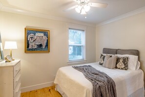 A bedroom with a bed, a window, a ceiling fan, a nightstand, and a painting. - Fairhope Downtown Cottage Sleeps 10  "Walk to Town" Lots of Parking and Garage (Fairhope)