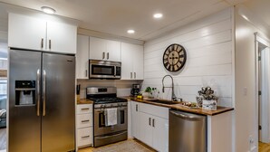 Una cocina moderna con electrodomésticos de acero inoxidable, armarios blancos, encimera de madera y un reloj de pared.