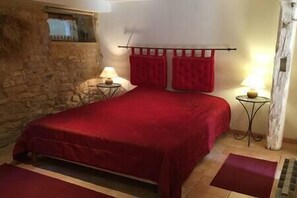 Cozy retreat with a large bed, stone wall, and a small table with a lamp.