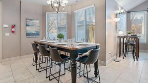 A dining area with a large table, chairs, a chandelier, and a fire extinguisher on the wall.