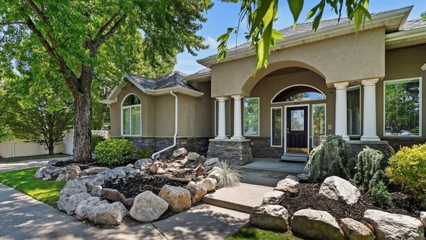 A two-story house with a stone facade, a front porch with columns, and a landscaped front yard with rocks and shrubs.