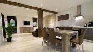 A modern kitchen with a stone wall, wooden beams, and a dining area with a table and chairs.