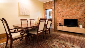 A dining area with a brick wall, a television, and a patterned rug.