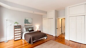 A bedroom with a bed, bedside tables, a floor lamp, a potted plant, a painting, and a wardrobe.