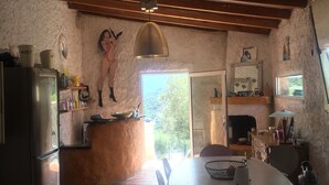 A kitchen with a refrigerator, a dining table with chairs, a hanging pendant light, and a view through a window. - Typical Corsican property, 3 bedrooms sleeps 6, view of the Gulf of Porto (Osani)
