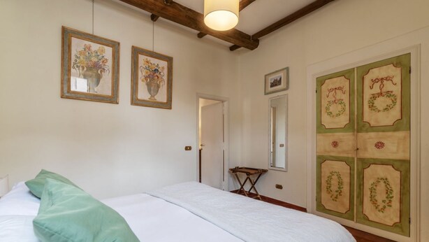 Ein Schlafzimmer mit einem Bett, einem grünen Kopfkissen, Holzboden, einem Spiegel und einer Tür mit dekorativen Feldverzierungen.