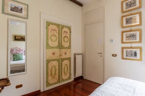 Een kamer met een bed, een garderobe met decoratieve panelen, een radiator en ingelijste afbeeldingen aan de muur.