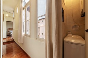 A hallway with wooden flooring, white walls, and a window with a curtain.