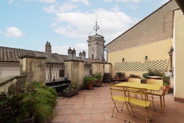 A courtyard with a yellow table and chairs, surrounded by potted plants and a tiled floor.