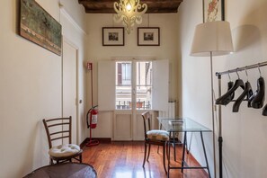 A narrow hallway with wooden flooring, a glass table, two chairs, a fire extinguisher, and a coat rack.