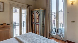 Ein Schlafzimmer mit Bett, Kleiderschrank, Stuhl und einem Balkon mit Blick auf Gebäude.