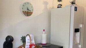 Keittiössä on musta työtaso, valkoiset kaapit, seinällä oleva kello, jääkaappi ja pieni kasvi sen päällä.